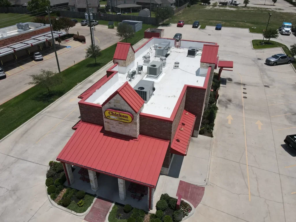 Aerial view of a Chicken Express restaurant with a bright red roof and brick exterior, surrounded by a parking lot.