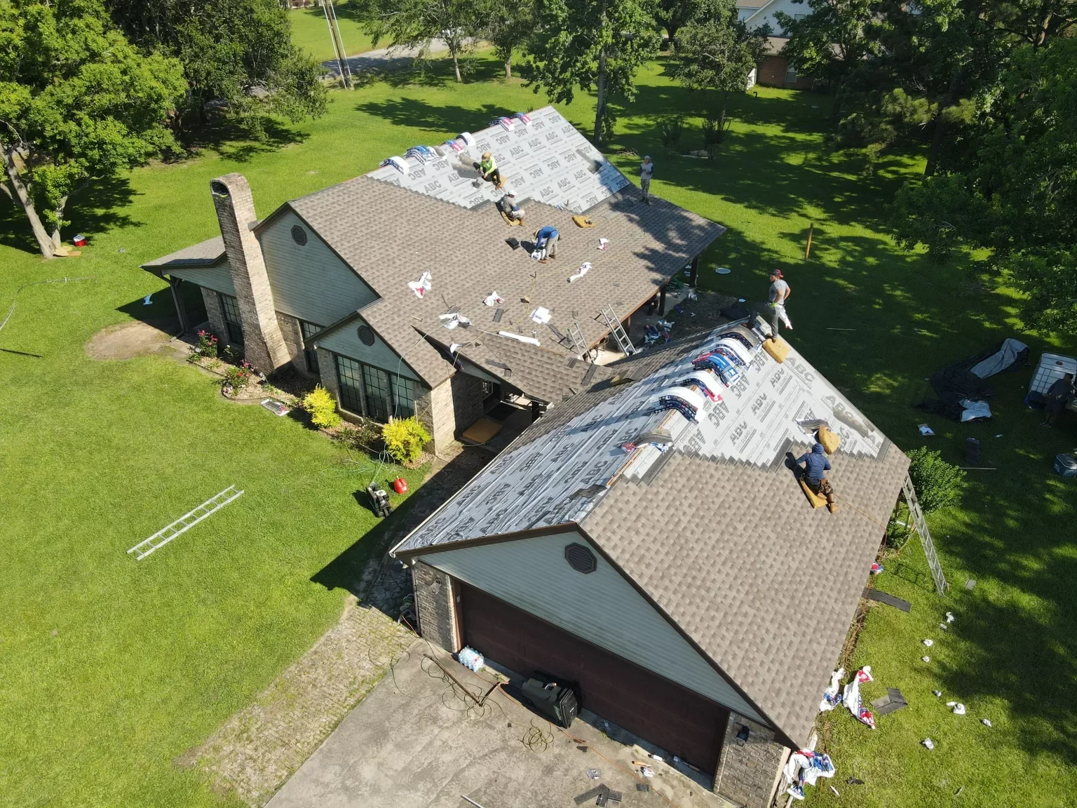 Aerial view of roofers installing new shingles and underlayment on a large residential house.