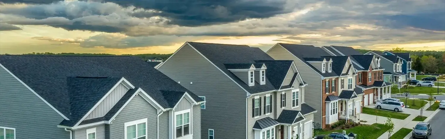 Aerial view of a row of modern suburban houses under a dramatic cloudy sky at sunset.