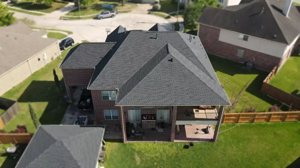 A modern gray house with dark shingle roof, stone accents, white trim, and a small tree in front.