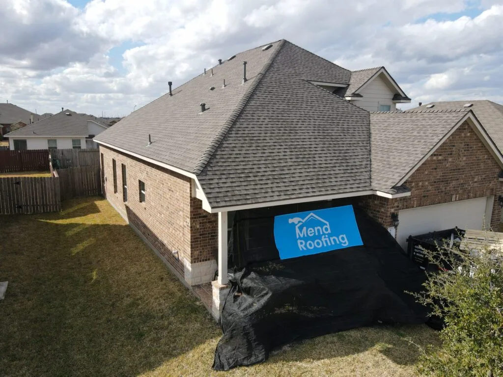 Overhead view of a house with a newly shingled roof, a blue 'Mend Roofing' sign, and a large black tarp.
