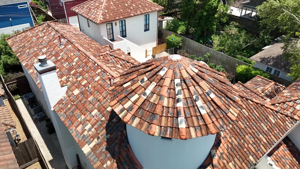 Aerial view of a house with multi-toned clay tile roofs, including a round section, and a white chimney.