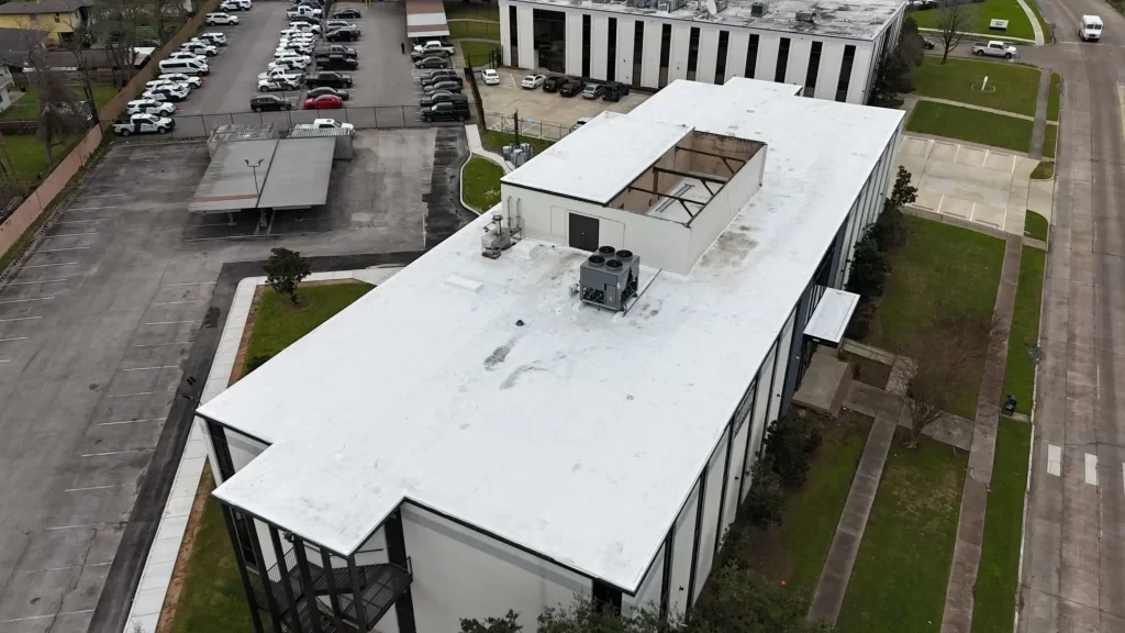 Aerial view of a white, grey, and blue office building with a 'For Lease' sign, surrounded by parking lots and residential houses.