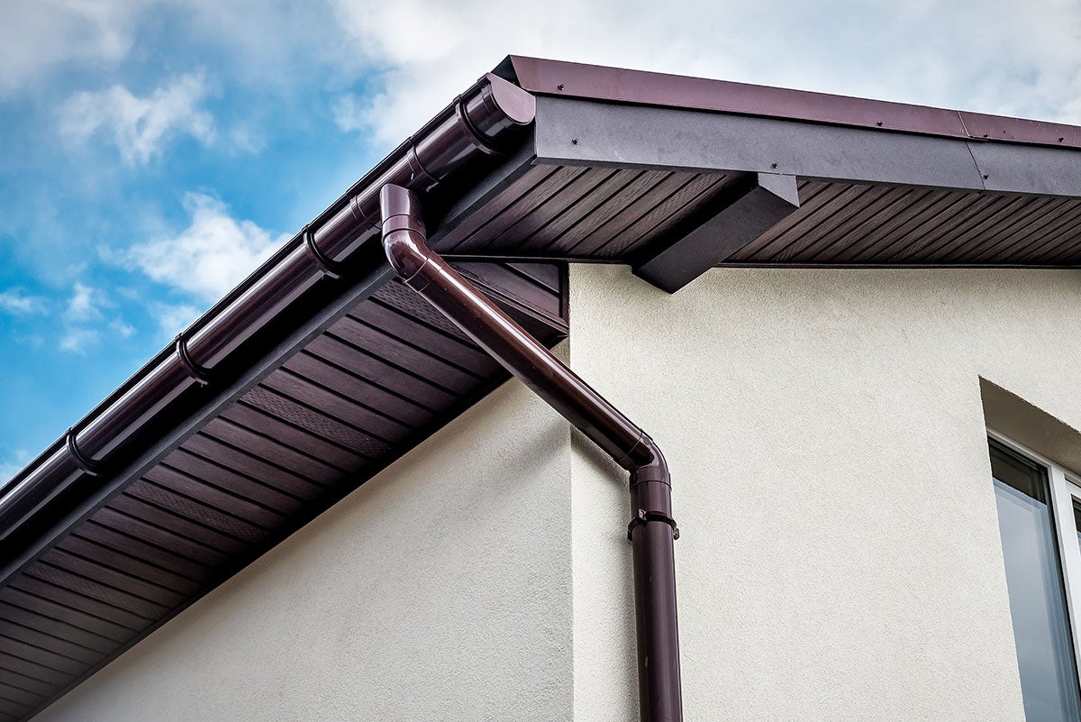 Brown gutters against a beige house and blue sky. The underside of the eaves is dark brown.